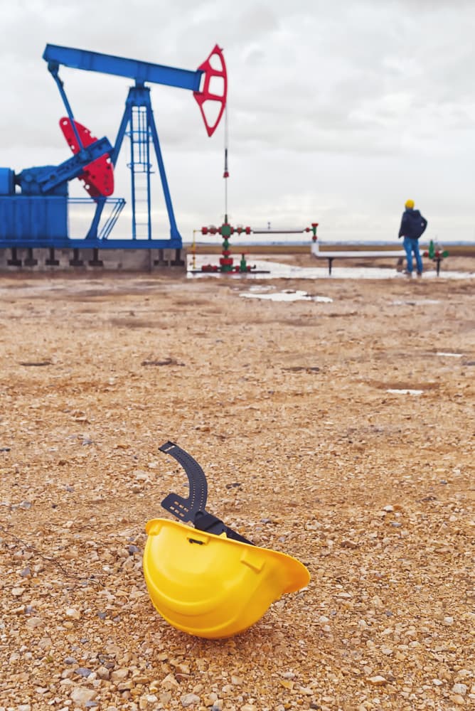 Protective Industrial Safety Helmet and Pumpjack Oil Pump operating on natural gas in the field pumping from the oil well.