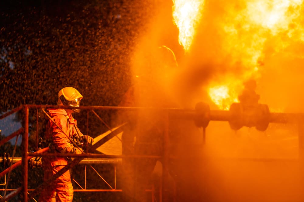 Firefighter using water fog type fire extinguisher to fighting with the fire flame from oil pipeline leak and explosion on oil rig and natural gas station.