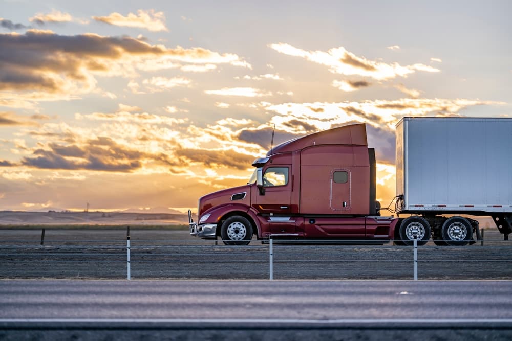 Industrial long hauler big rig burgundy semi truck tractor on a highway 