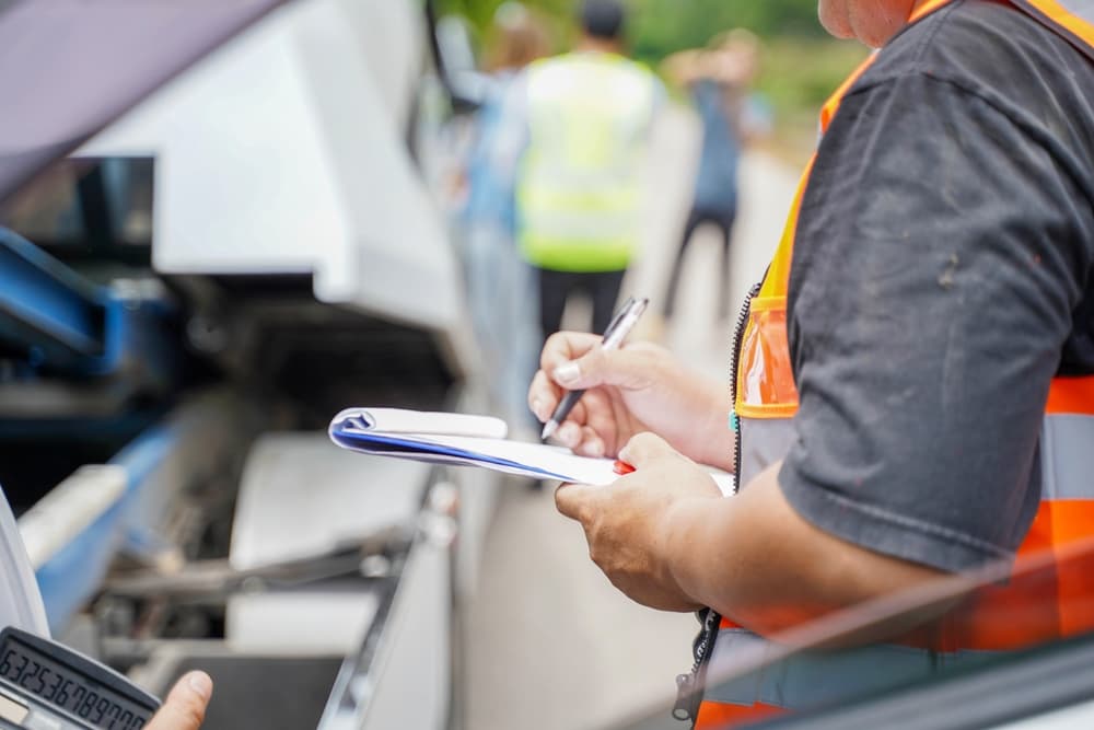 Insurance agent writing on clipboard while examining truck after accident 