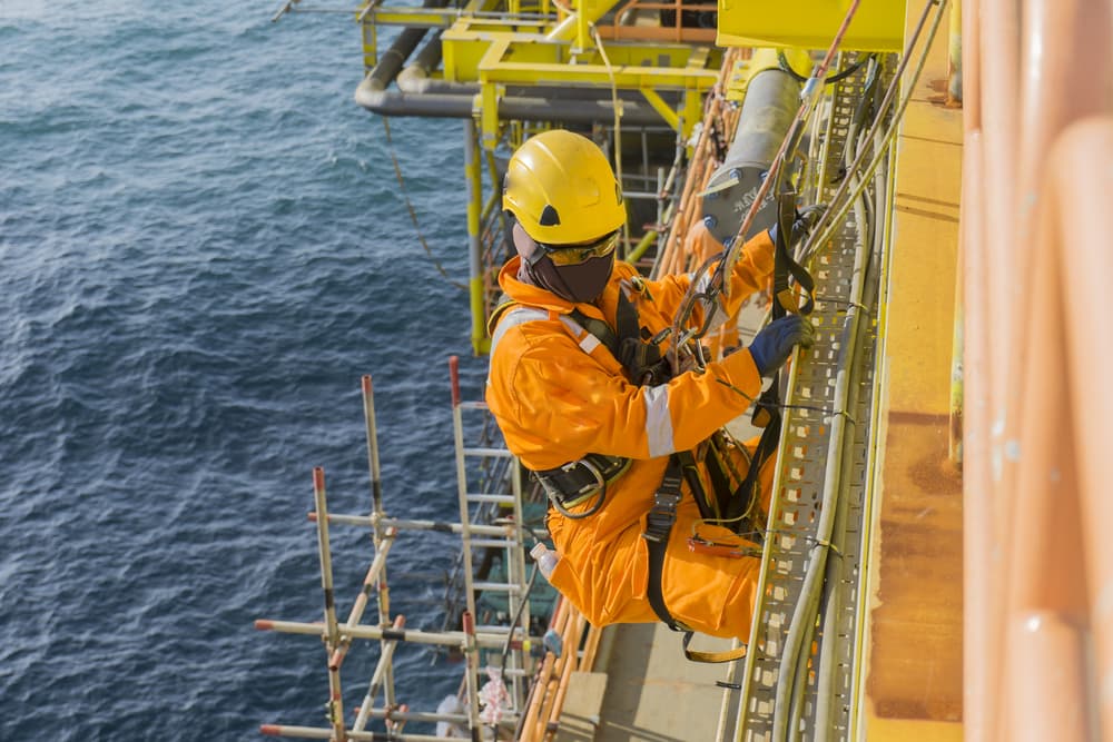 Man working overboard with personal protective equipment (PPE) climbing and hanging at the edge of oil and gas rig platform in the middle of sea.